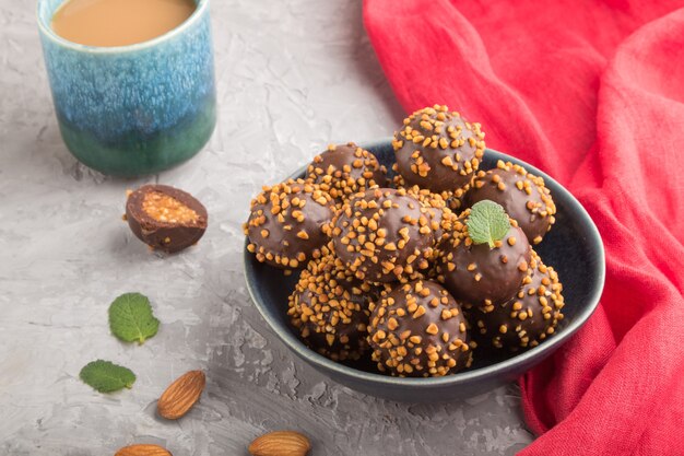 Schokoladen-Karamell-Ball-Bonbons mit Mandeln und einer Tasse Kaffee auf grauer Betonoberfläche und rotem Textil