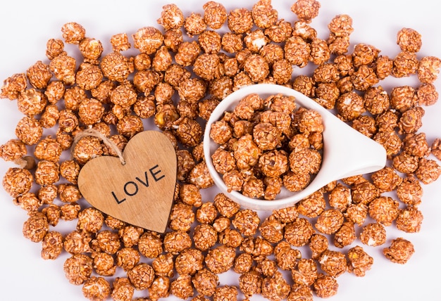 Foto schokoladen-karamell-popcorn in der weißen tasse und im hölzernen herzen