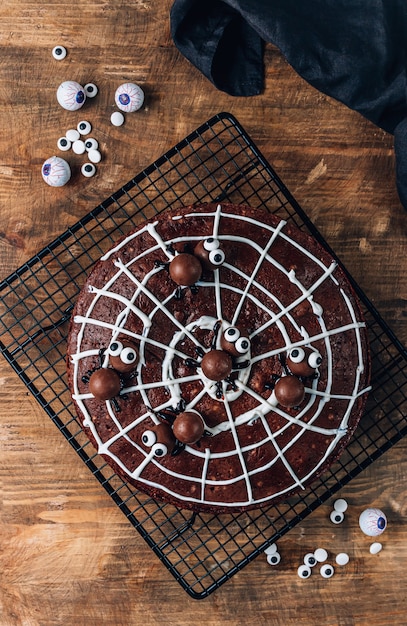 Schokoladen-Spinnennetz-Brownies mit Süßigkeitenspinnen, hausgemachte Leckereien für Halloween auf rustikalem Holzhintergrund