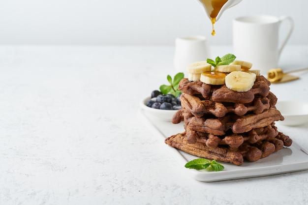 Schokoladenbananenwaffeln mit ahornsirup auf weißer tabelle, kopienraum, seitenansicht. süßer brunch