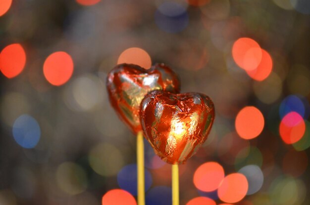 Schokoladenbonbons zum Valentinstag Rote Herzformschokolade auf Lolly-Stick Schokoladenherz in roter Folie auf einem Stick auf Bokeh verschwommenem Hintergrund