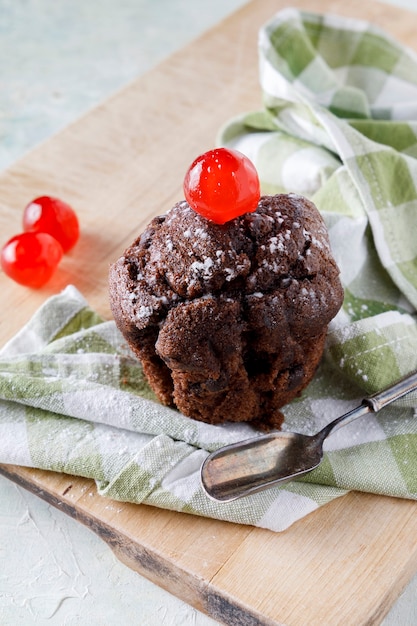 Schokoladencupcake mit Zuckerguss auf Serviette auf Holzbrett und altem Löffel