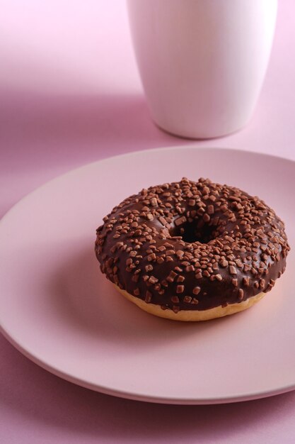 Schokoladendonut mit Streuseln auf Platte nahe Tasse Kaffee, süß glasiertem Dessertessen und heißem Getränk auf rosa minimalem Hintergrund, Winkelansicht-Makro