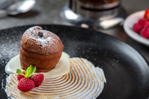 Schokoladenfondantkuchen mit Vanillecreme, Himbeere und Minze auf einem schwarzen Teller