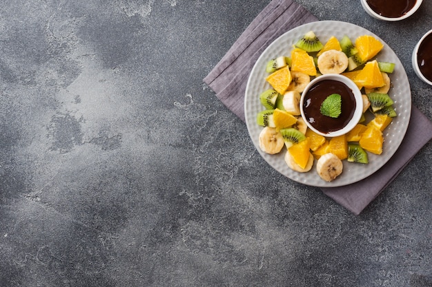 Schokoladenfondue mit Früchten auf dunklem Beton