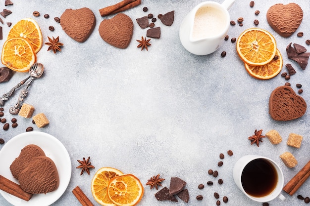 Schokoladenherzplätzchen, Orangenzimt und würzige Gewürze auf einem grauen Tisch, Draufsicht, Kopienraum.