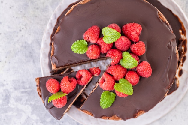 Schokoladenkäsekuchen mit frischen Himbeeren und Minzblättern. Ein Stück Kuchen wird geschnitten und auf einem Teller serviert. Hausgemachtes Dessert. Nahansicht.