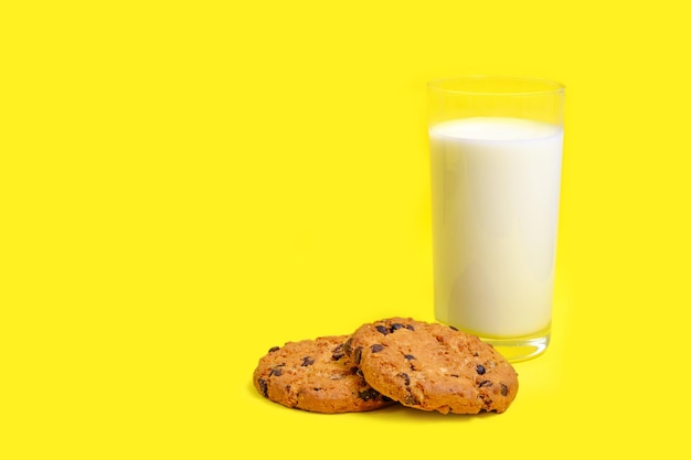 Schokoladenkekse und ein Glas Milch auf einem leuchtend gelben Hintergrund.