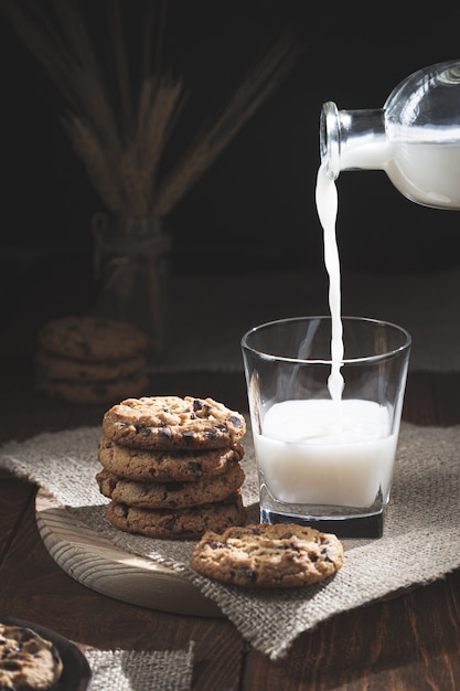 Schokoladenkekse und Milchflasche, die Milch in einem Glas auf einem Holzfuß verschüttet