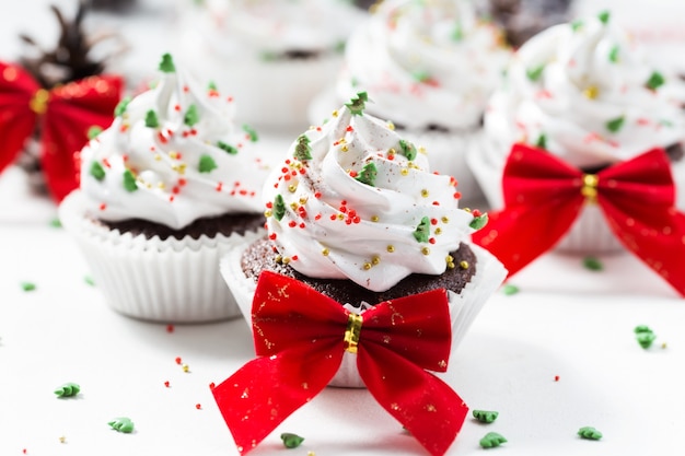 Schokoladenkleine kuchen verzierten weiße Sahne- und Tannenbäume auf einer weißen Platte. Weihnachtssüßigkeiten. Neujahrsdessert