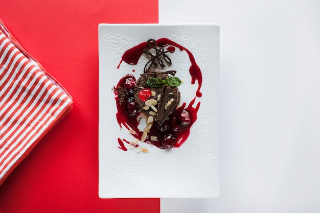 Schokoladenkuchen auf buntem Hintergrund aus Rot und Weiß Köstliches Dessert im Restaurant mit Dekoration aus Kirschmandel und Minzdraufsicht mit freiem Platz