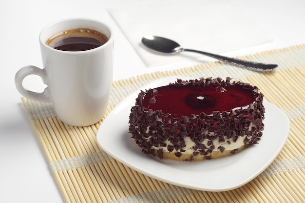 Schokoladenkuchen mit Kirschgelee und Tasse Kaffee auf Bambusserviette
