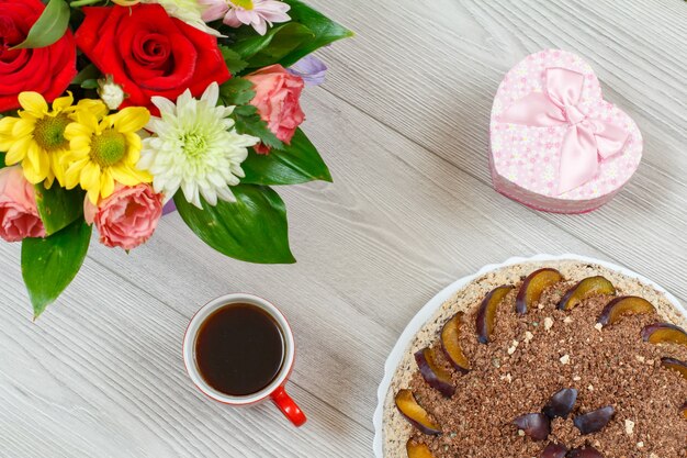 Schokoladenkuchen mit Pflaumen, einem Blumenstrauß, einer Geschenkbox und einer Tasse Kaffee