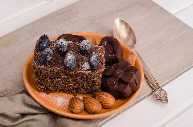 Schokoladenkuchen, Muffin mit Pralinen, verziert mit Beeren, Puderzucker und Mandeln auf einer Tontasse auf einem weißen Holztisch