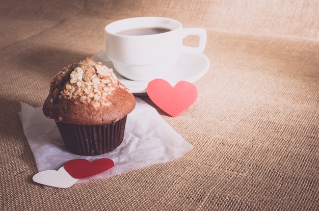 Schokoladenmuffin und Kaffee und Herzen auf Sackleinenbeschaffenheiten