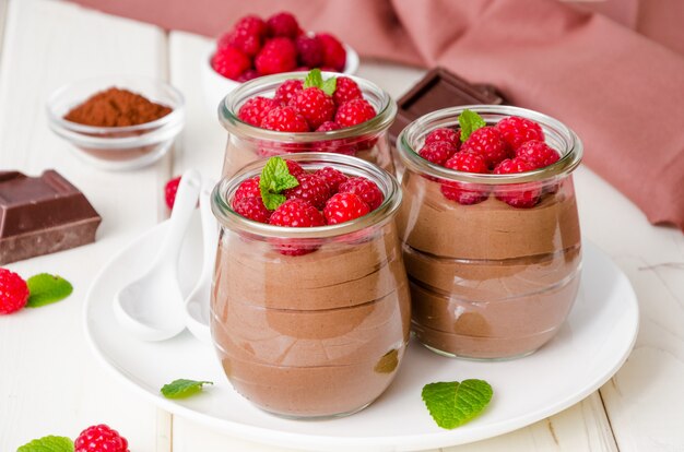 Schokoladenpudding (Kremeis) mit frischen Himbeeren in den Glasgefäßen auf einem weißen Holz