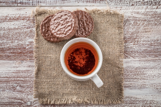 Schokoladensplitterplätzchen und ein Becher Tee auf weißem Holztisch.