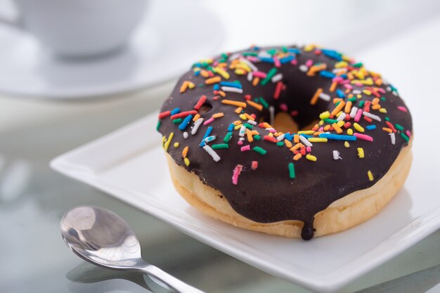 Schokoladenstreusel Donut auf einem weißen Teller und einer Tasse Kaffee