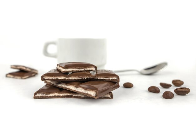 Schokoladenstücke und eine Tasse Kaffee auf weißem Hintergrund