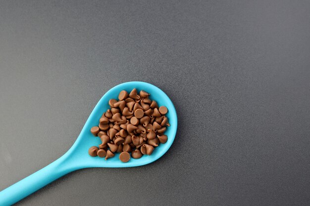 Foto schokoladentropfen in einem blauen löffel auf grauem hintergrund. streusel zum dekorieren von süßwaren.