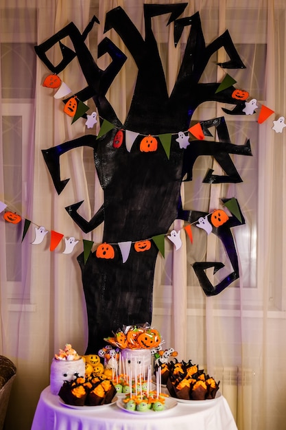 Schokoriegel mit Süßigkeiten zur Feier von Halloween. Riesiger schwarzer Baum mit Dekorationen auf dem Hintergrund