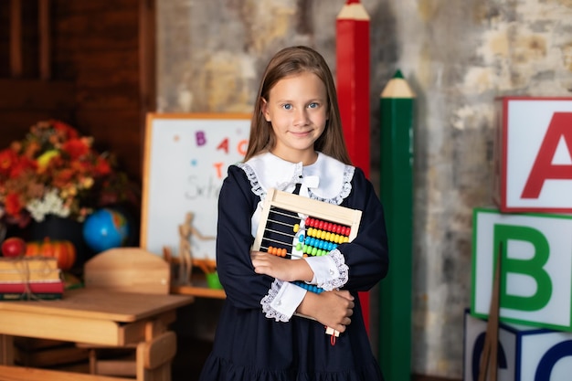 School Girl in dress sostiene un colorido puesto de ábaco cerca de la pizarra en la escuela.