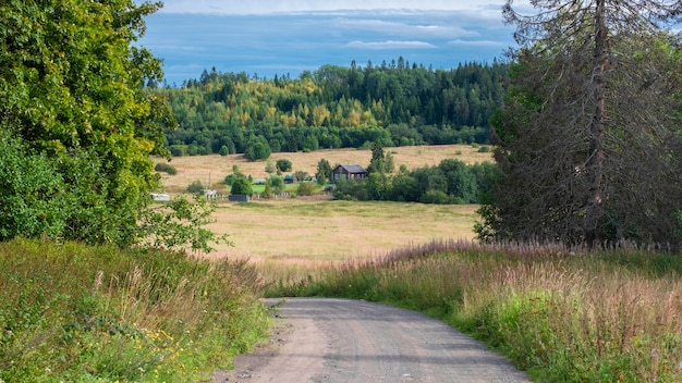 Schotterstraße zwischen Feldern und Wäldern, die zu einem Dorf führt