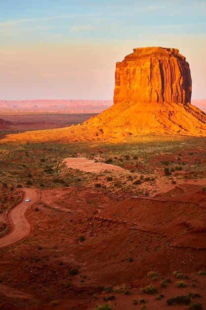 Schotterweg mit Auto neben großer roter Felsensäule rot im Monument Valley-Sonnenuntergang