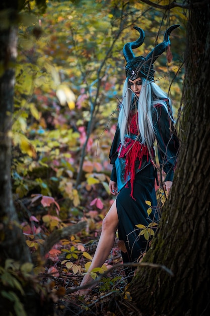 Schreckliche Frau mit Hörnern und erstaunlichem Make-up nahe dem Baum im Wald