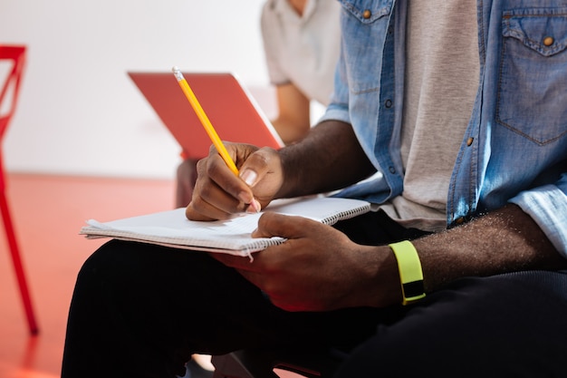 Schreiben. Nahaufnahme der Hände eines jungen Studenten, der an der Vorlesung sitzt und notwendige Notizen in seinem Notizbuch macht