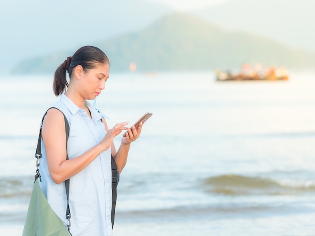 Schreibender Handy der asiatischen netten Frau für ihre Jobs beim Reisen in dem Meer