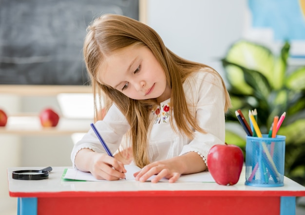 Schreibensklassenarbeit des kleinen blonden Mädchens im Schulklassenzimmer