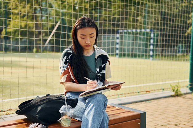 Schreibt in den Notizblock Junge asiatische Frau ist tagsüber im Freien