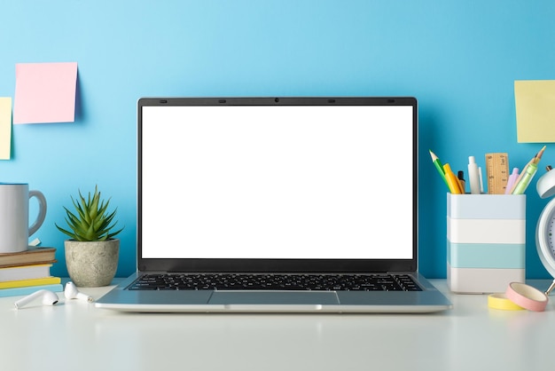 Schreibtisch des Schülers während des Online-Bildungskonzepts Seitenansicht Foto eines weißen Schreibtisches mit Laptop und Schreibzeug auf isoliertem blauen Hintergrund mit Copyspace für Text oder Werbung
