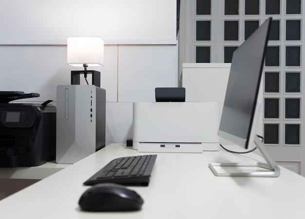 Schreibtisch mit einem schwarz-grauen PC, einem Schwarz-Weiß-Drucker und einem Bildschirm
