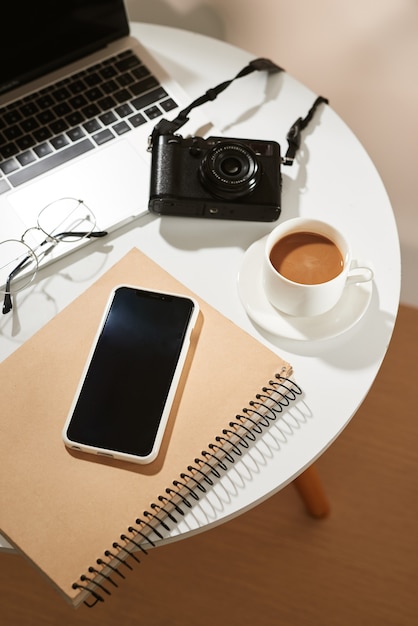 Schreibtisch mit Handy, Kaffeetasse, Laptop, Kamera und Brille