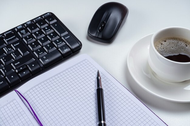 Schreibtisch Schreibtisch. Arbeitsplatz mit leerem Notizbuch, Tastatur, Bürobedarf und Kaffeetasse auf weißem Hintergrund.