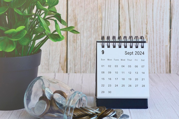 Schreibtischkalender für September 2024 mit Münzstapel und Topfpflanze auf einem Holzschreibtisch