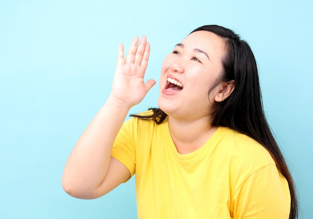 Schreiende und Hand Porträt-Asien-Frau auf seinem Mund, lokalisiert auf blauem Hintergrund im Studio.