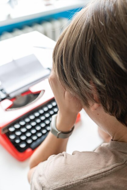 Foto schriftstellerin, die nachdenklich an einem buch auf ihrer roten schreibmaschine arbeitet