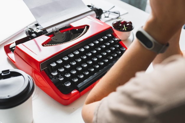 Schriftstellerin, die nachdenklich an einem Buch auf ihrer roten Schreibmaschine arbeitet