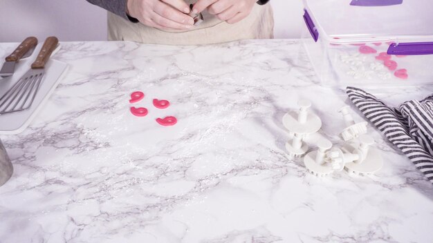 Schritt für Schritt. Ausstechen von Schneeflocken mit Ausstechformen aus rosafarbenem Fondant auf einer Marmortheke.