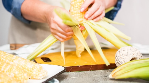 Schritt für Schritt. Bio-Mais schälen, um mexikanischen Maiskolben Elote herzustellen.