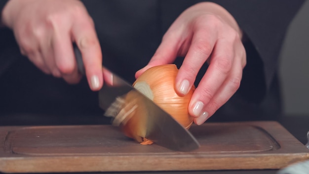 Schritt für Schritt. Gelbe Zwiebel auf einem Holzschneidebrett würfeln.