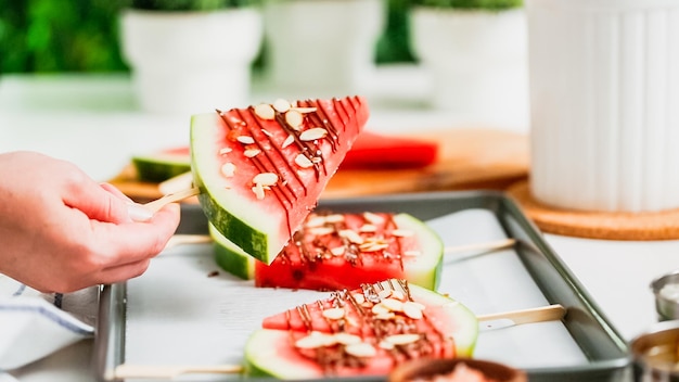 Schritt für Schritt. Mit Schokolade und Meersalz garnierte Wassermelonenspalten auf dem Stiel auf dem Backblech.