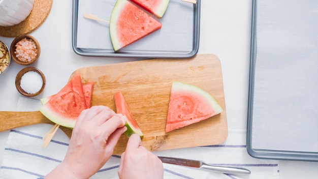 Schritt für Schritt. Schieben Sie den Holzknallstab in den Wassermelonenlohnkeil, um Wassermeloneneis zu machen.