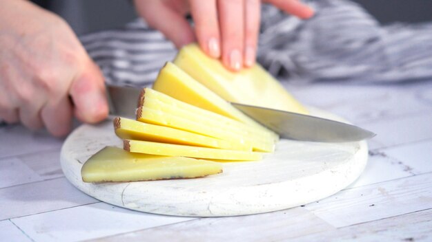 Schritt für Schritt. Schneiden eines Gourmet-Käses auf einem weißen Schneidebrett mit einem Küchenmesser.