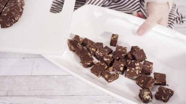 Schritt für Schritt. Schneiden von hausgemachtem Macadamia-Fudge auf einem weißen Schneidebrett.