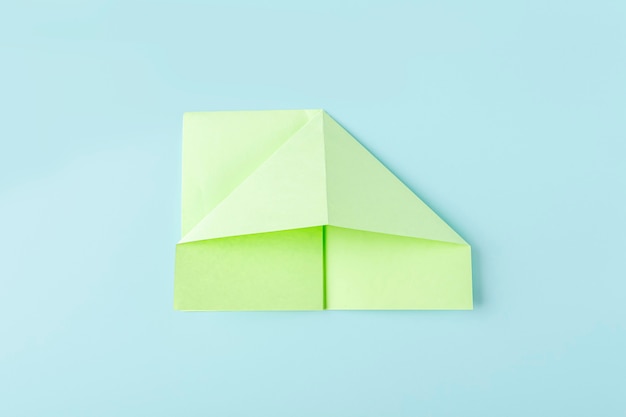 Schritt zwei, wie man einen Origami-Papierschmetterling mit grünem Papier, Schere auf blauem Hintergrund macht