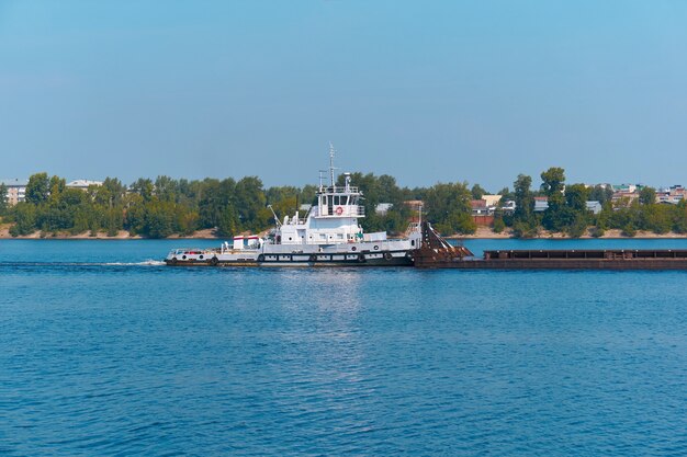 Schubboot schiebt Trockenschüttgutkahn auf dem Fluss an der Stadtküste vorbei